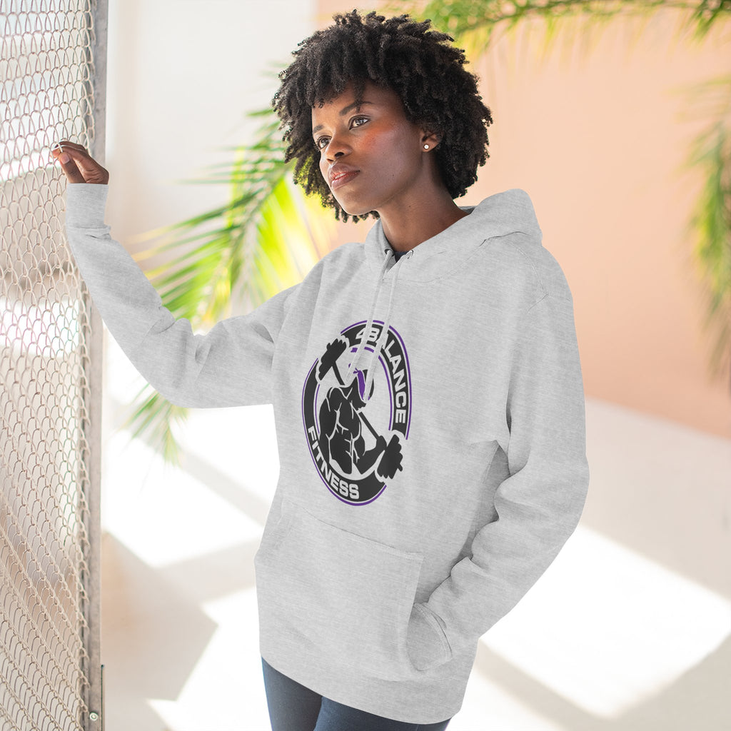 Person wearing a gray hoodie with a logo, standing against a light background with plants.