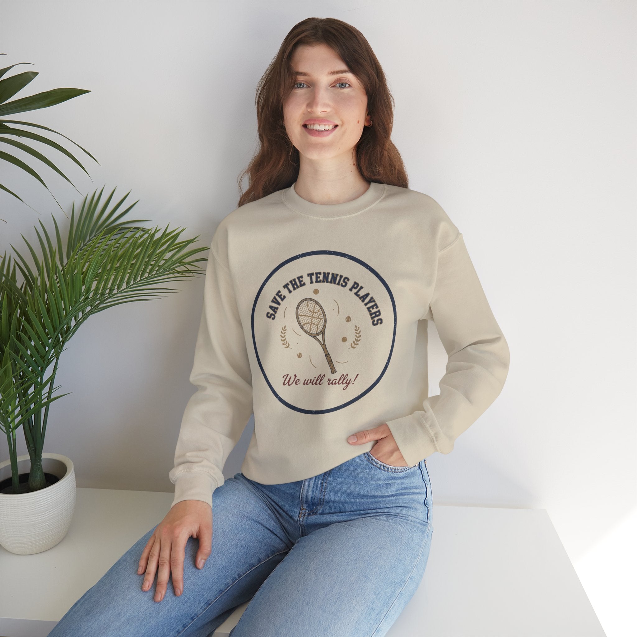 Woman wearing a beige sweatshirt with a graphic design sitting on a white surface with a plant in the background.
