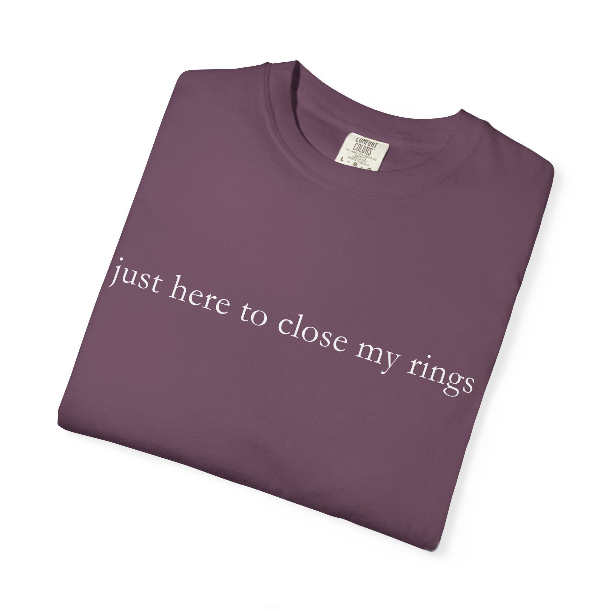 Folded purple t-shirt with text 'just here to close my rings' on a white background