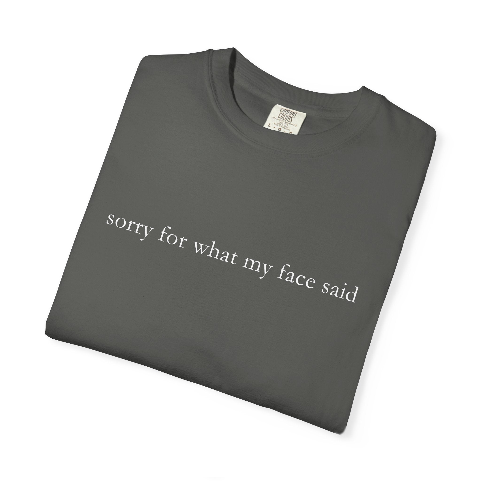 Folded dark gray t-shirt with text 'sorry for what my face said' on a white background